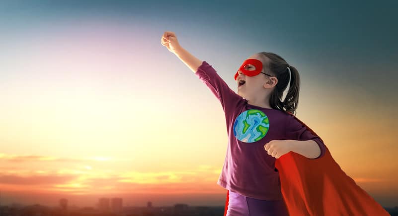 Earth day concept. Child superhero with symbol of ecological worldviews on sunset cityscape background.